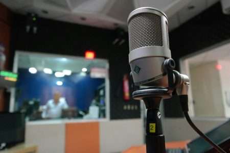 Close-up of a microphone in a recording studio with a blurred sound engineer in the background.