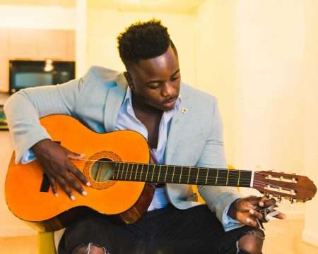 A focused man tunes his acoustic guitar indoors, creating an artistic musical ambiance.